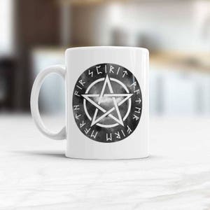 Może przedstawiać: Biały kubek ceramiczny z czarno-białym wzorem pentagramu. Pentagram otoczony jest okręgiem z napisami "FIRE, WATER, EARTH, AIR, SPIRIT" napisanymi w runach wokół zewnętrznej krawędzi.