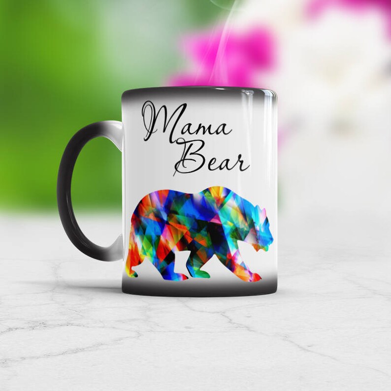 May include: A black and white color changing mug with the text "Mama Bear" in black lettering. The mug features a colorful abstract bear design.