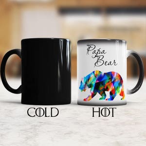 May include: A black and white color changing mug with the text "Papa Bear" and a colorful bear design. The mug is black when cold and reveals the design when hot.