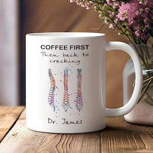 May include: White coffee mug with the text "COFFEE FIRST Then back to cracking" and a colorful illustration of three spines. The mug is personalized with the name "Dr. James".