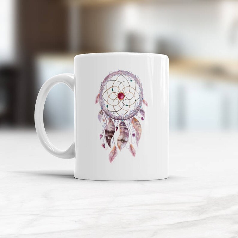 May include: White ceramic mug with a colorful dreamcatcher design. The dreamcatcher has a brown and gold circular frame with feathers in shades of pink, purple, and brown.
