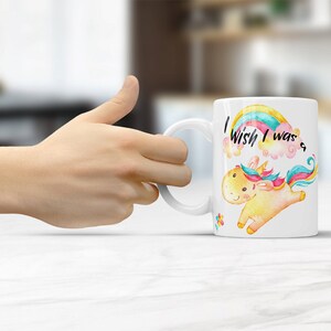 May include: White ceramic mug with a colorful rainbow and a unicorn illustration. The text on the mug reads "I wish I was a..."
