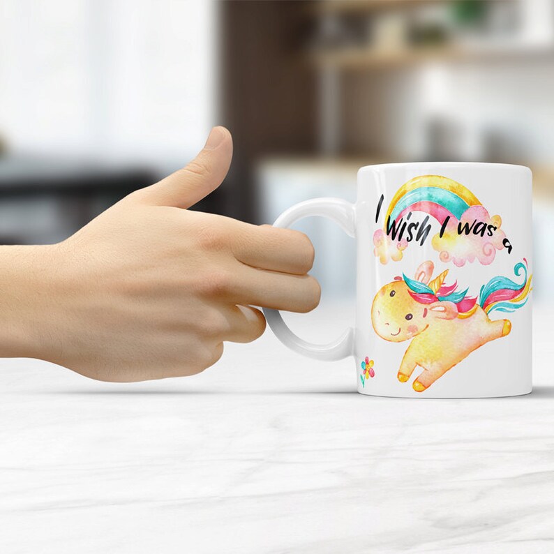 May include: White ceramic mug with a colorful rainbow and a unicorn illustration. The text on the mug reads "I wish I was a..."