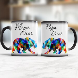 May include: Two black ceramic mugs with white interiors. The mug on the left has the text "Mama Bear" and the mug on the right has the text "Papa Bear". Both mugs feature a colorful bear silhouette.