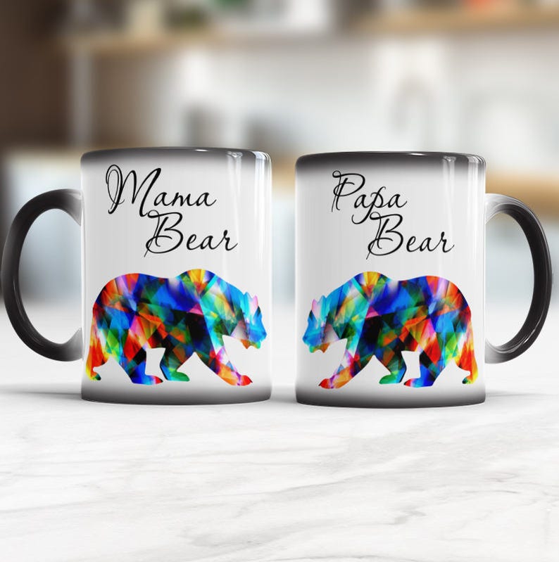 May include: Two black ceramic mugs with white interiors. The mug on the left has the text "Mama Bear" and the mug on the right has the text "Papa Bear". Both mugs feature a colorful bear silhouette.
