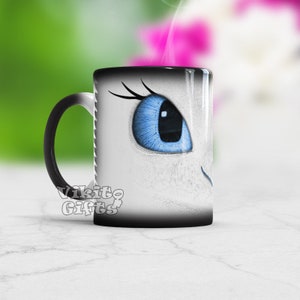 Peut inclure: Une tasse à changement de couleur noire et blanche avec un gros plan sur l'œil bleu d'un dragon blanc. La tasse porte le texte "Vikito Gifts" au bas.