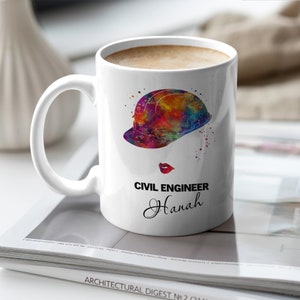 Op de afbeelding: Witte keramische mok met een kleurrijke aquarel-illustratie van een helm en de tekst "CIVIL ENGINEER Hannah".