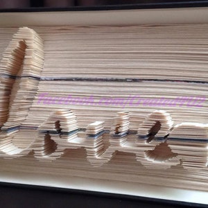 May include: A book with the word "Love" folded into the pages. The pages are folded to create the letters of the word. The book is closed and the spine is visible.
