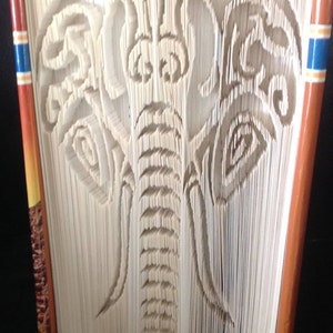 May include: A book with the pages folded to create a 3D elephant design. The elephant is white and the book cover is brown with a colorful stripe on the spine.