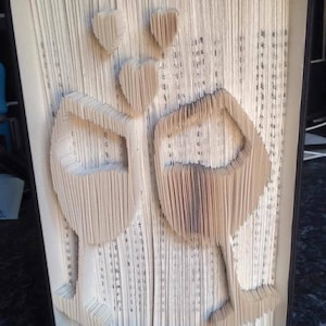 May include: A book art sculpture of two wine glasses with hearts above them. The sculpture is made from the pages of a book that have been folded and cut to create the design.