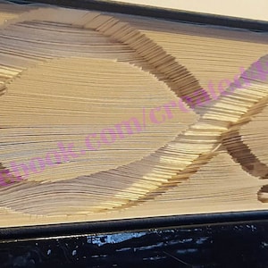 May include: A book with an infinity symbol and the word "Love" carved into the pages. The pages are a light tan colour, and the edges are cut to form the design. The book has a black cover and is displayed on a dark surface.