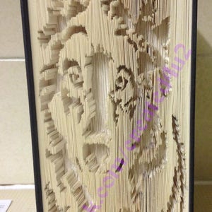 May include: A book with pages folded into a 3D design of a flower. The book is bound in black and the pages are a cream colour.