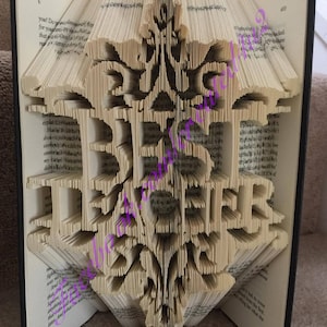 May include: A book with pages folded into a 3D design of a decorative floral pattern. The book is open and the pages are folded to create a raised, intricate design.