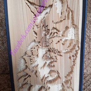 Può includere: Un libro con le pagine piegate per creare una scultura 3D della testa di un gatto. La scultura è fatta di carta ed è di colore marrone chiaro.