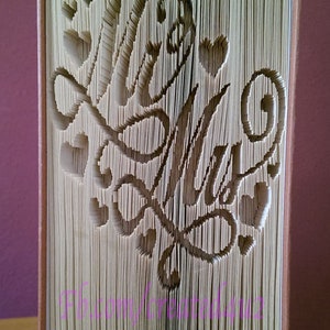 Può includere: Una scultura di arte di libro con le parole "Mr. & Mrs." piegate nelle pagine. Il libro è beige e le parole sono ritagliate dalle pagine.