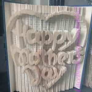 May include: A book with the words "Happy Birthday to You" folded into the pages in the shape of a heart. The book is bound in blue and has a white cover.