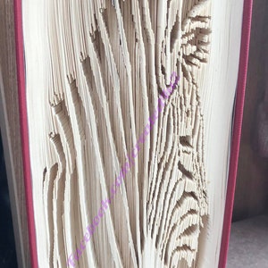 May include: A book with a red cover has been folded into the shape of a zebra. The pages are folded into a 3D design.