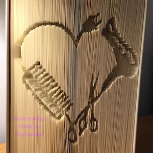 Könnte beinhalten: Ein Buch, das zu einem Herz gefaltet ist, mit einer Schere und einem Kamm im Inneren. Das Buch ist beige und der Text auf dem Rücken ist sichtbar: "Fb.com/created4u2 @created4u2 Etsy/Created4u2"