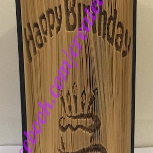 May include: A brown book with the words "Happy Birthday" carved into the cover. The book is folded into a three-dimensional design that resembles a birthday cake with candles.