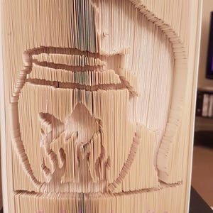 May include: A book folded into the shape of a 3D image of a bird. The book is made of white paper and the bird is in a light brown color.