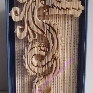 May include: A book art sculpture of a seahorse made from the pages of a book. The pages are folded and layered to create a 3D effect. The sculpture is displayed on a blue book cover.