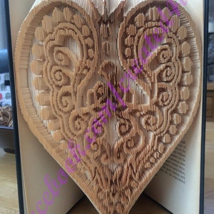 May include: A book with pages folded into a three-dimensional heart shape. The heart is made of paper and has a detailed, intricate design.