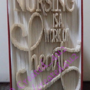 Op de afbeelding: Een wit boek met de woorden "Nursing is a work of heart" gevouwen in de pagina's. Het boek is gebonden in een rode kaft.