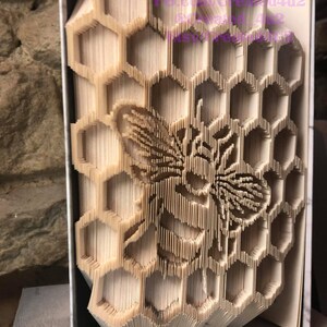 May include: A book folded into a 3D sculpture of a honeycomb with a bee in the center. The sculpture is made of paper and is a light brown color.