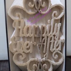 May include: A book with the words "Happily Ever After" folded into the pages. The book is open and the folded pages are visible. The book is white and the words are in a white font.