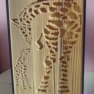 Könnte beinhalten: Eine Buchkunstskulptur aus einer Giraffe und einem Seepferdchen, die durch Falten der Seiten eines Buches hergestellt wurde. Die Skulptur besteht aus beigefarbenem Papier und wird auf einer weißen Oberfläche präsentiert.