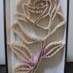 May include: A white book with the pages folded to create a 3D rose. The rose is in the center of the book and has a stem and leaves.