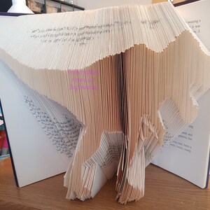 May include: A book folded into the shape of a dinosaur. The dinosaur is standing on a wooden surface. The book is open and the pages are visible.