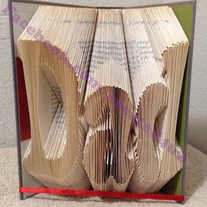 May include: A book art sculpture of the word "DAD" created by folding the pages of a book. The book is bound in a gray and green cover and has a red ribbon tied around it.