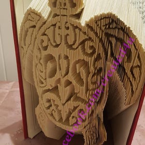 May include: A book with pages folded into a 3D sculpture of a turtle. The sculpture is made from the pages of a book and is a unique and creative way to display a book.