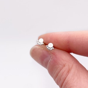May include: A pair of silver stud earrings with a small, round, white stone in the center and a circle of smaller silver beads around the stone.