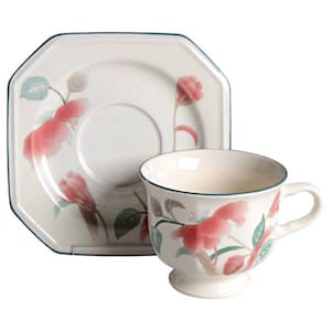May include: A cream-colored teacup and saucer set. The cup has a handle and sits on a small pedestal. Both pieces are decorated with pink floral designs and green leaves. The edges are trimmed with a dark blue line.