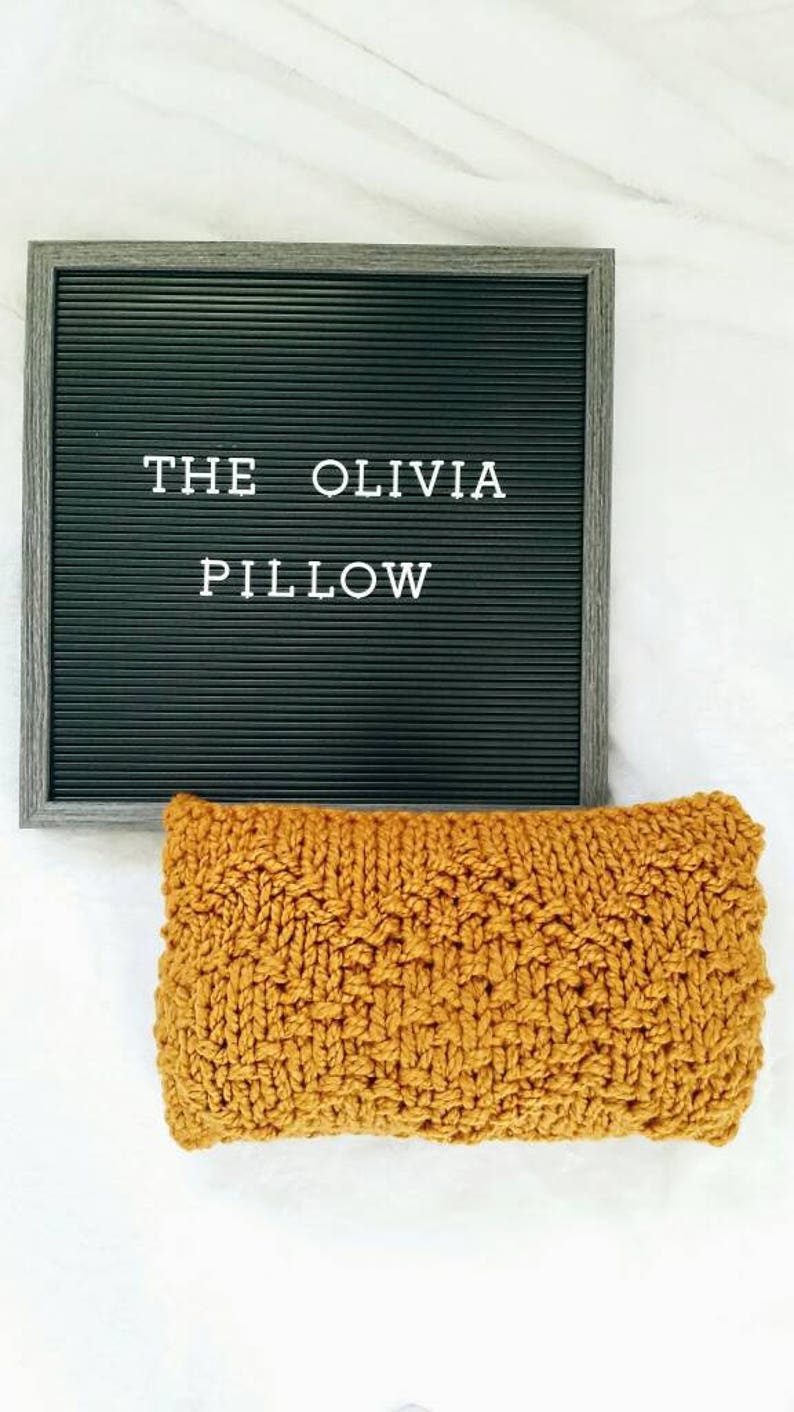 May include: A mustard yellow knitted pillow with the text "THE OLIVIA PILLOW" on a black letter board behind it.