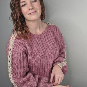 May include: A pink crocheted sweater with white crocheted trim on the sleeves. The sweater has a relaxed fit and a slightly cropped length.