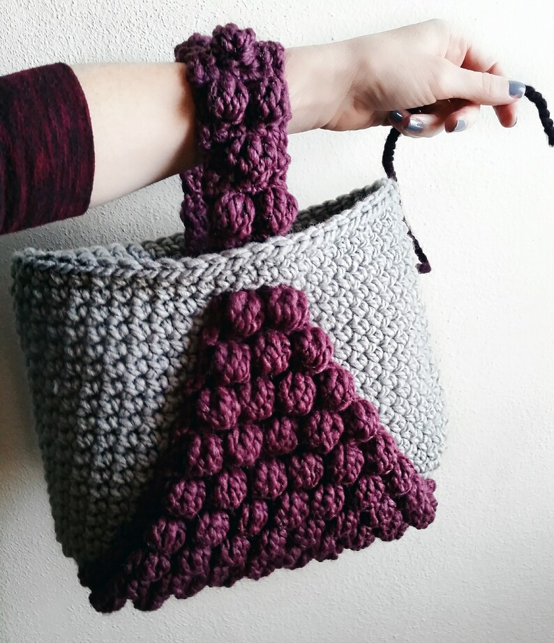 May include: A gray crocheted tote bag with a burgundy crocheted handle and a burgundy crocheted triangle design on the front.