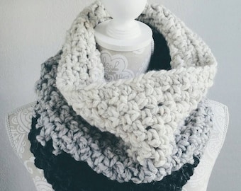 May include: A crocheted infinity scarf in three shades of grey, from white to black. The scarf is made with a chunky yarn and has a textured stitch.