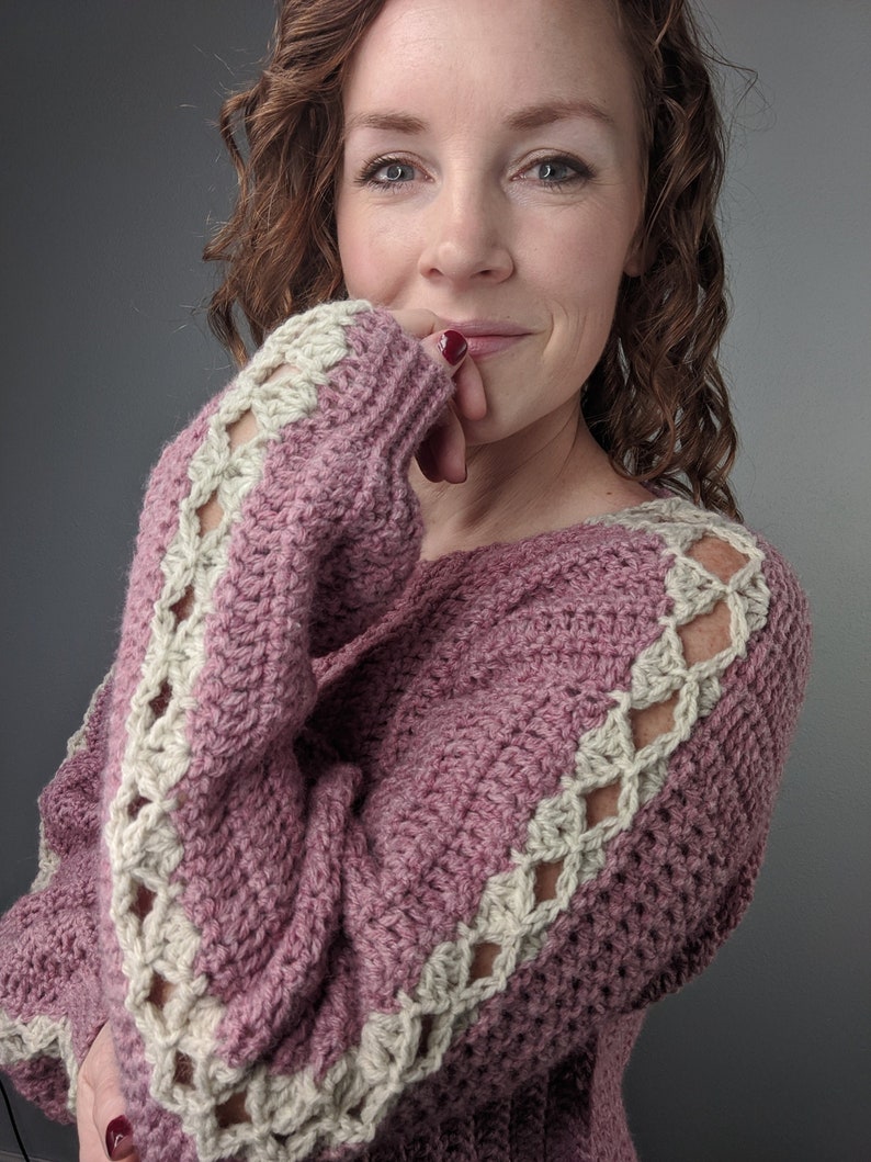 May include: A pink crocheted sweater with a white crocheted trim around the sleeves and neckline.