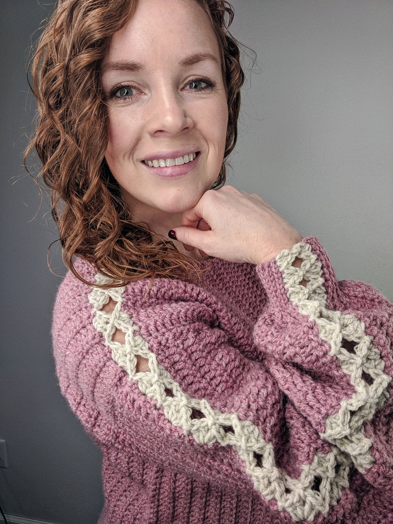 May include: A pink crocheted sweater with a white crocheted trim around the sleeves and shoulders.