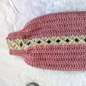 May include: A pink crocheted garment with a beige crocheted trim. The garment has a textured, woven appearance.