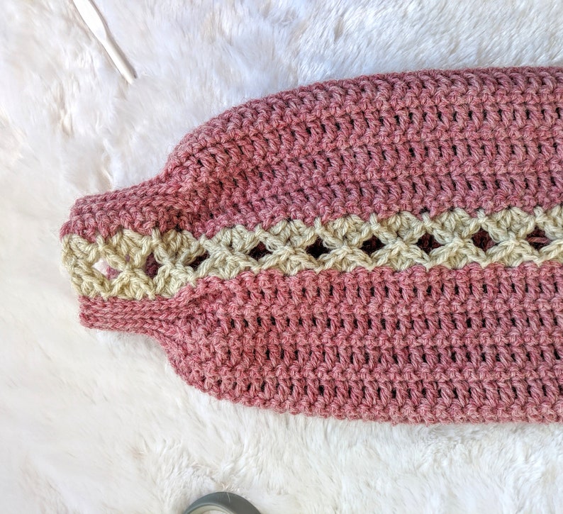 May include: A pink crocheted garment with a beige crocheted trim. The garment has a textured, woven appearance.