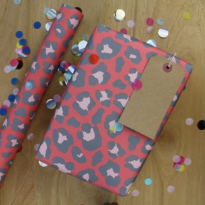 May include: Pink and gray leopard print wrapping paper with a brown gift tag. The wrapping paper is surrounded by colorful confetti.