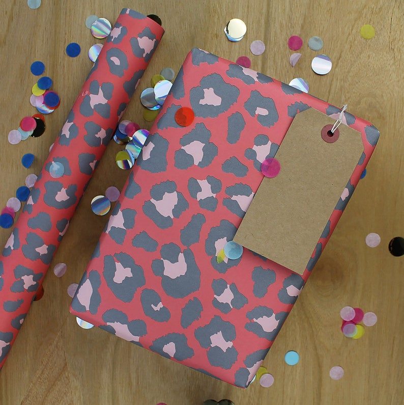 May include: Pink and gray leopard print wrapping paper with a brown gift tag. The wrapping paper is surrounded by colorful confetti.