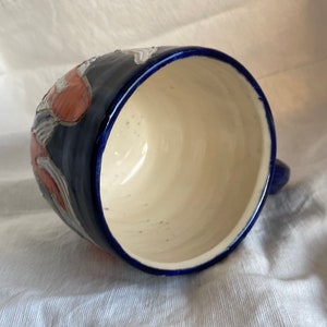 Pu&ograve; includere: Una tazza in ceramica con esterno blu scuro e interno color crema. La tazza ha un manico ed &egrave; decorata con disegni floreali rossi e bianchi. Il bordo e il manico sono anch'essi blu scuro.