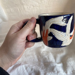 Pu&ograve; includere: Tazza in ceramica blu scuro con un motivo floreale bianco e arancione. La tazza ha un interno bianco e un manico blu scuro. Il motivo floreale &egrave; in rilievo.