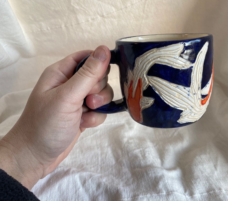 Pu&ograve; includere: Tazza in ceramica blu scuro con un motivo floreale bianco e arancione. La tazza ha un interno bianco e un manico blu scuro. Il motivo floreale &egrave; in rilievo.