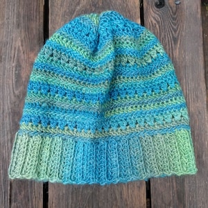 May include: A blue and green crocheted beanie hat with a striped pattern. The hat is made with a soft yarn and has a comfortable fit.